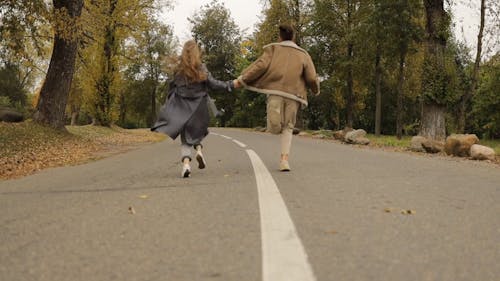 A Couple Running while Holding Hands in a Park