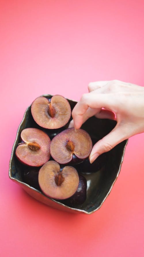 A Person Putting Slices of Plum in a Square Bowl