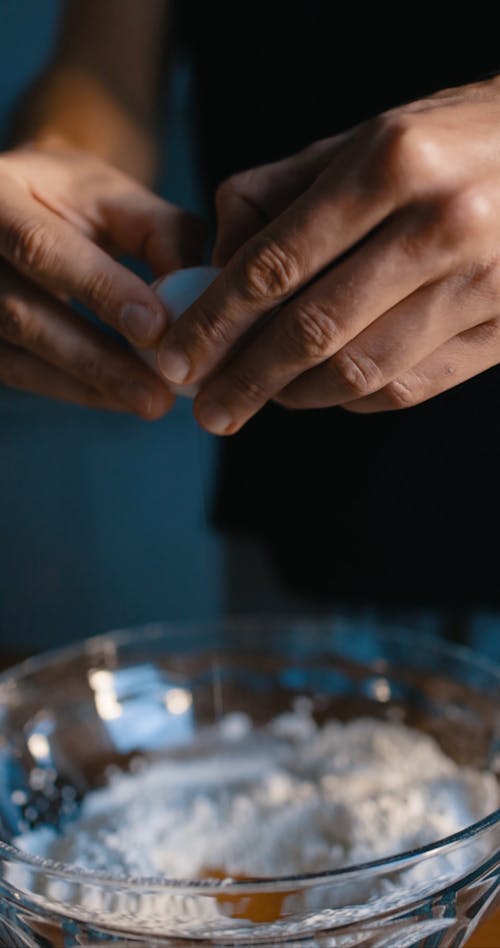 A Person Crackling an Egg into a Bowl of Flour