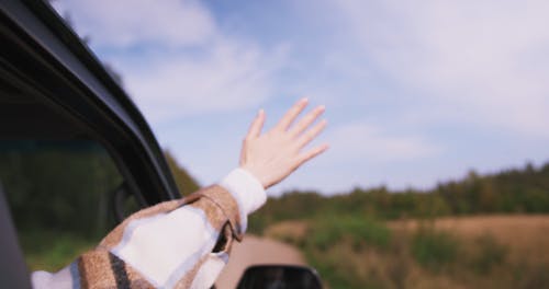 A Person Riding on a Car While Waving Outside the Window