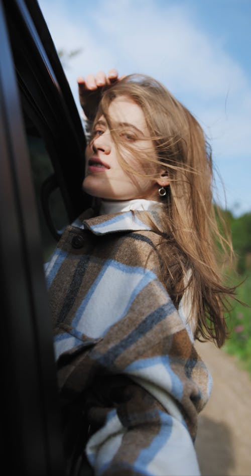 A Woman Enjoying the Sun and the Wind Outside the Window of a Moving Car