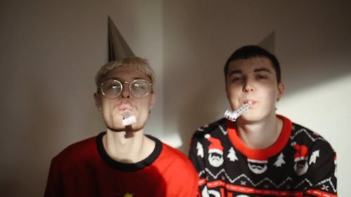 Two Men Blowing of Party Pipes While Wearing Party Hats