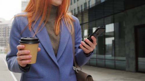 A Person Using Her Smartphone While Holding Her Coffee