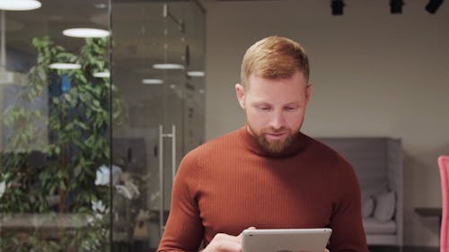 A Man Using a Tablet Computer While Walking Inside the Office