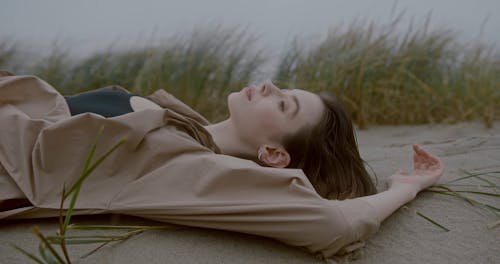 A Woman Lying Down on Sand While Looking Pensive