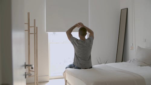 Person Sitting on His Bed While Stretching His Arms