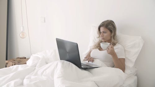 Donna Che Beve Il Suo Caffè Durante L'utilizzo Del Suo Computer Portatile