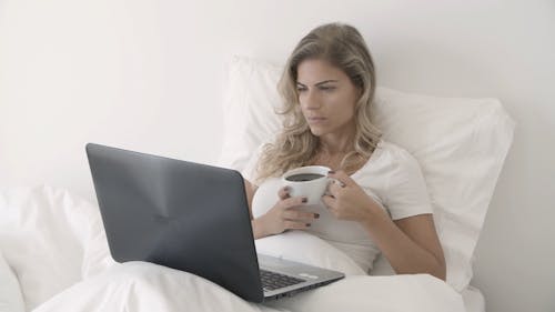 A Woman Having Coffee And Using Her Laptop In Bed