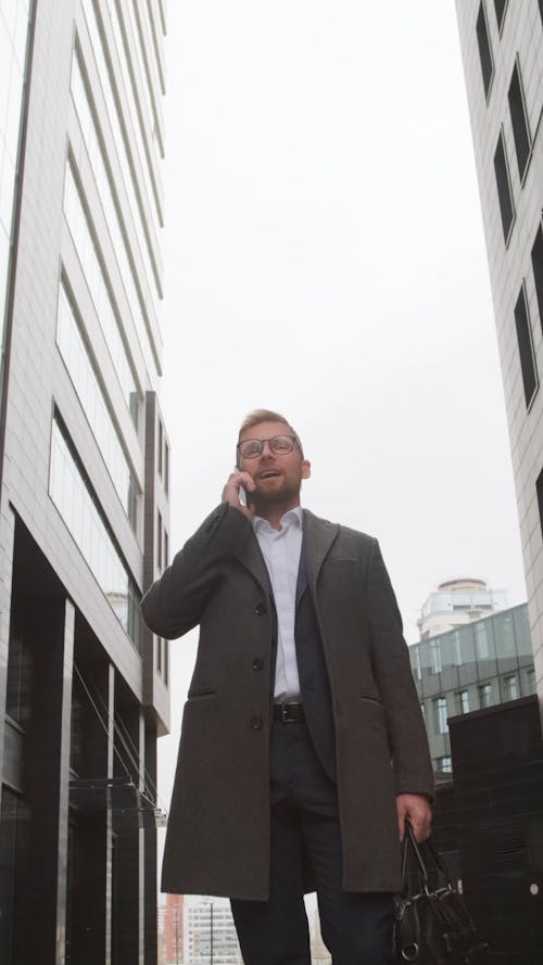 Man in Gray Coat Standing Outdoors While Talking on the Phone