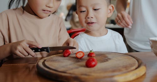 A Girl Slicing a Strawberry for Her Brother