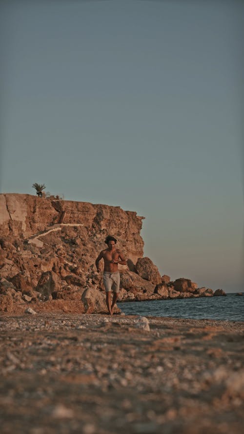 Vertical Video of a Man Jogging at the Seashore Barefooted