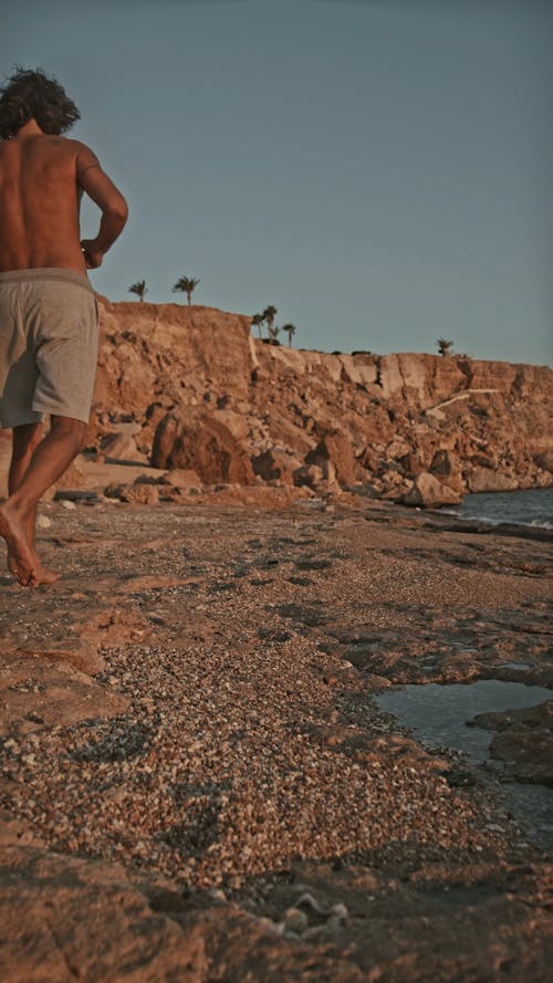 Vertical Video of a Man Jogging at the Seashore Barefooted