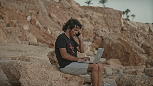 Man Sitting on a Rock While Using His Laptop and Smartphone