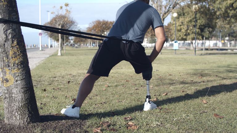Athlete with a prosthetic leg doing lunges with a resistance band in a park
