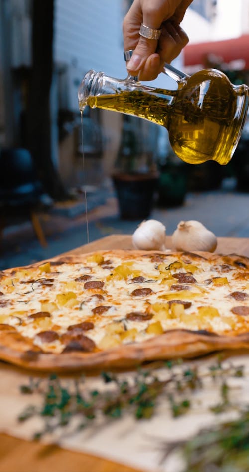 Person Adding Olive Oil on Top of Pizza