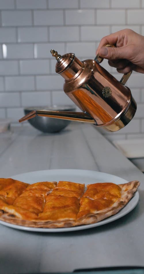 Person Pouring Oil on the Top of a Pizza