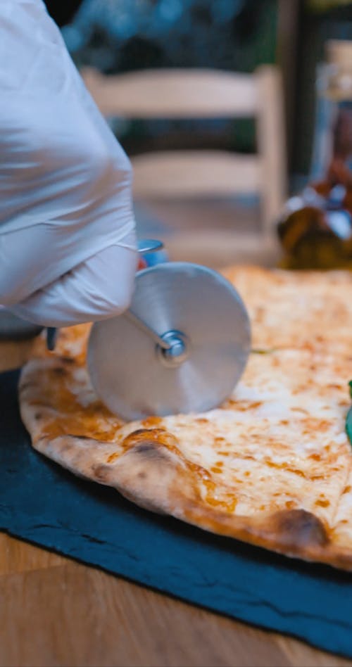 Person Slicing a Pizza with a Pizza Cutter