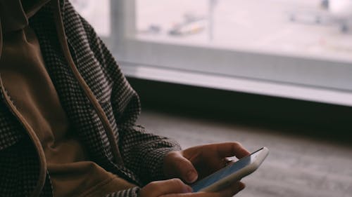 Person with Face Mask Using Smartphone in Airport