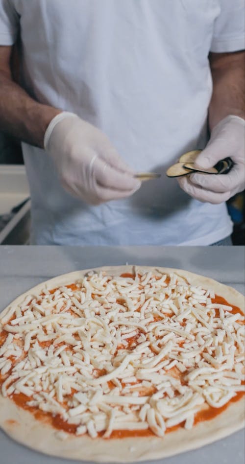 Person Putting Toppings on the Top of the Pizza