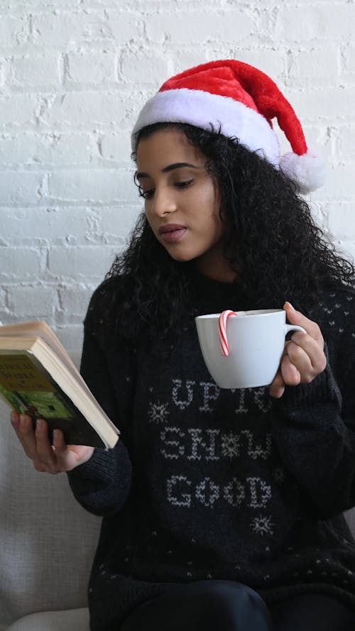 Young Woman With Santa Hat Reading a Book Drinking Hot Cocoa