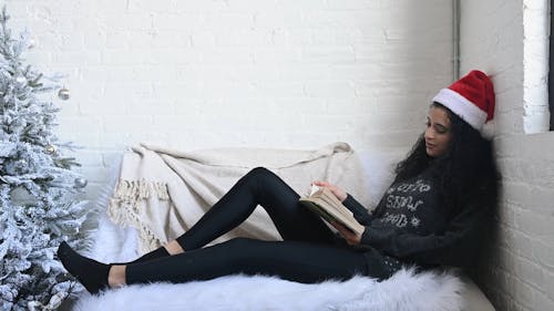 Girl on Christmas Hat Reading a Book on the Couch