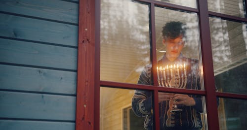 Young Man Holding Hanukkiah Looking Through Window 