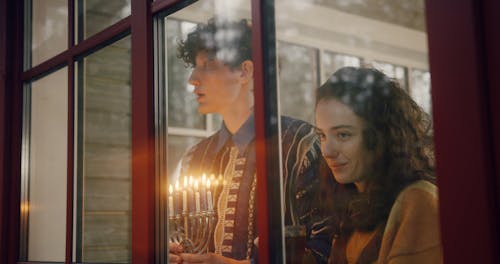 Man Holding Hanuka Candle While Chatting with the Woman Looking Through the Window