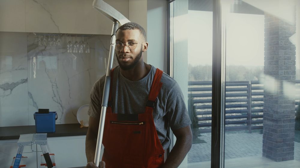 A window cleaner in red overalls holding a pole squeegee, smiling at the camera