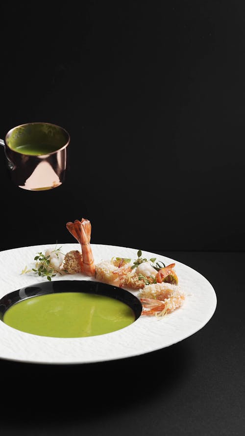 A Person Pouring a Green Soup on the Plate with Garnish on the Side