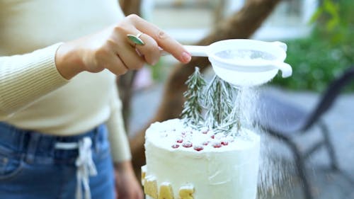Woman Sprinkles Icing Sugar Over a Cake