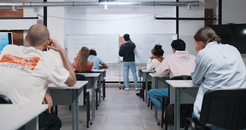 Back View of a Teacher Writing on a Whiteboard in the Class