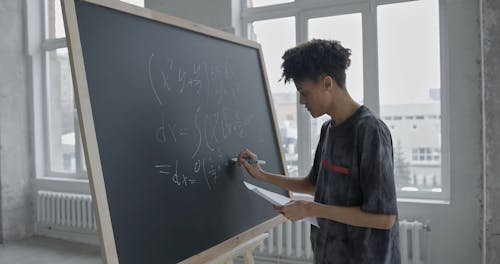 A Guy Writing Mathematical Equation on a Blackboard