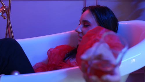 A Woman Holding and Drinking a Glass of Wine While in the Bathtub 