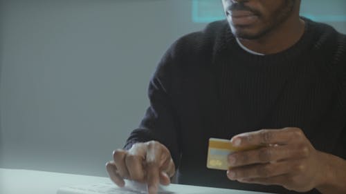 man Working on Computer with a Credit Card in Hand