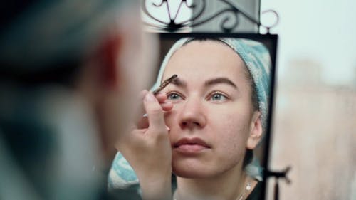 Woman Putting On Eyebrows in front of the Mirror