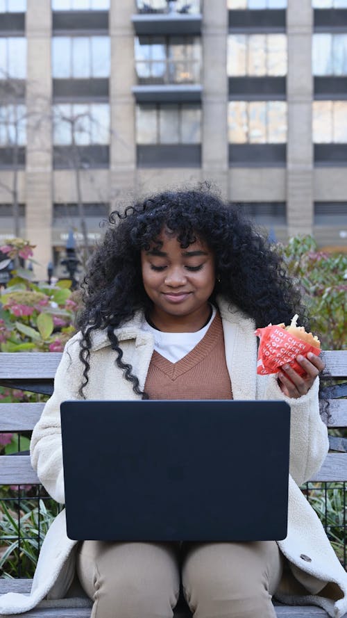 Woman Using Laptop While Eating a Burger