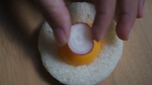 A Person Putting a Sliced Onion and a Parsley on Top of an Egg Yolk and Bread