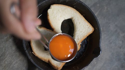 A Person Putting an Egg in the Middle of a Loaf Bread in a Frying Pan