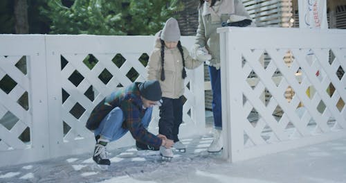 A Man Tying Ice Skating Shoelace of a Young Girl