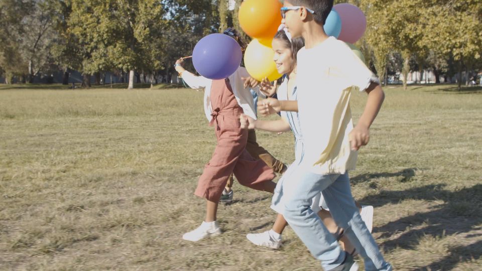 Children running across a meadow holding colourful balloons