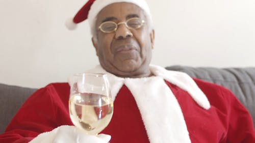 An Elderly Man Wearing Santa Costume Holding a Glass of Champagne and Drink it