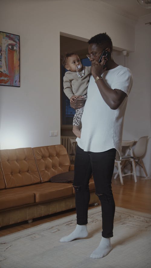 Man Talking On Phone While Hold Baby In Arms