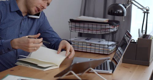 A Man Talking on His Phone While Typing on His Laptop