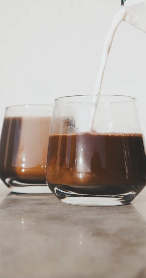 Pouring Milk into Black Coffee Glasses