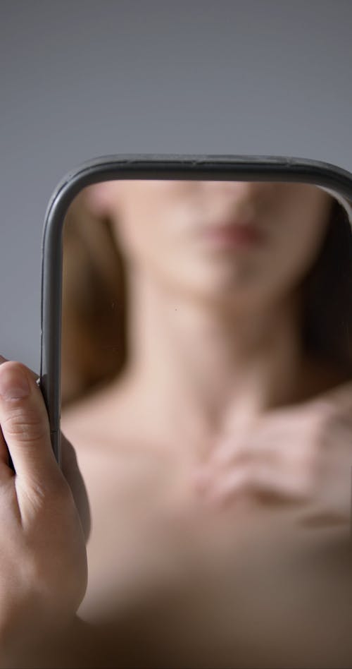 A Woman Holding a Mirror Reflecting Her Neck and Shoulders