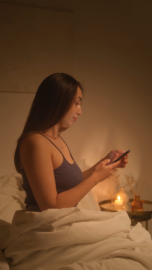 A Woman Texting While Sitting on the Bed