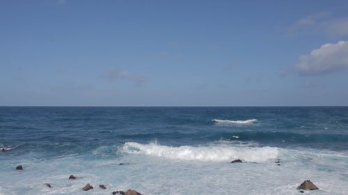 View of the Blue Ocean with Waves Splashing the Bed of Rocks