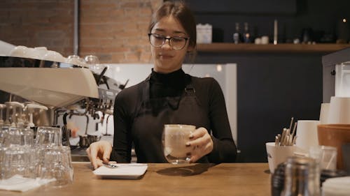 A Female Barista Serving Coffee on a Glass Cup