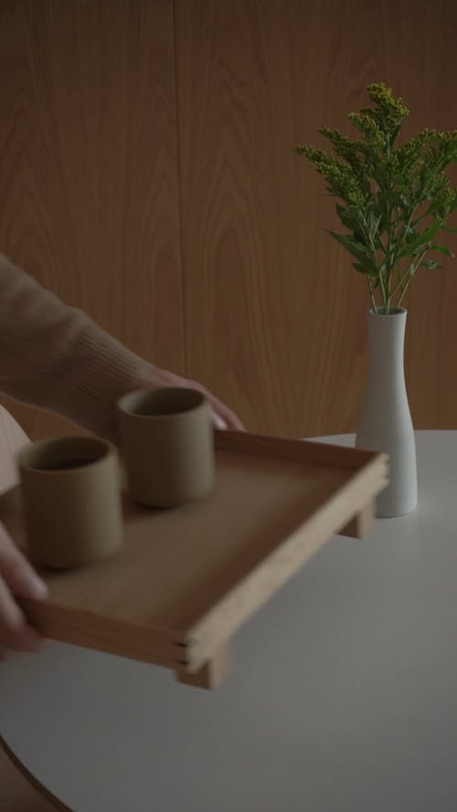 A Person Placing a Wooden Tray with Cups on a Table