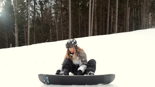 Female Snowboarder Fixing Straps of Her Snowboard